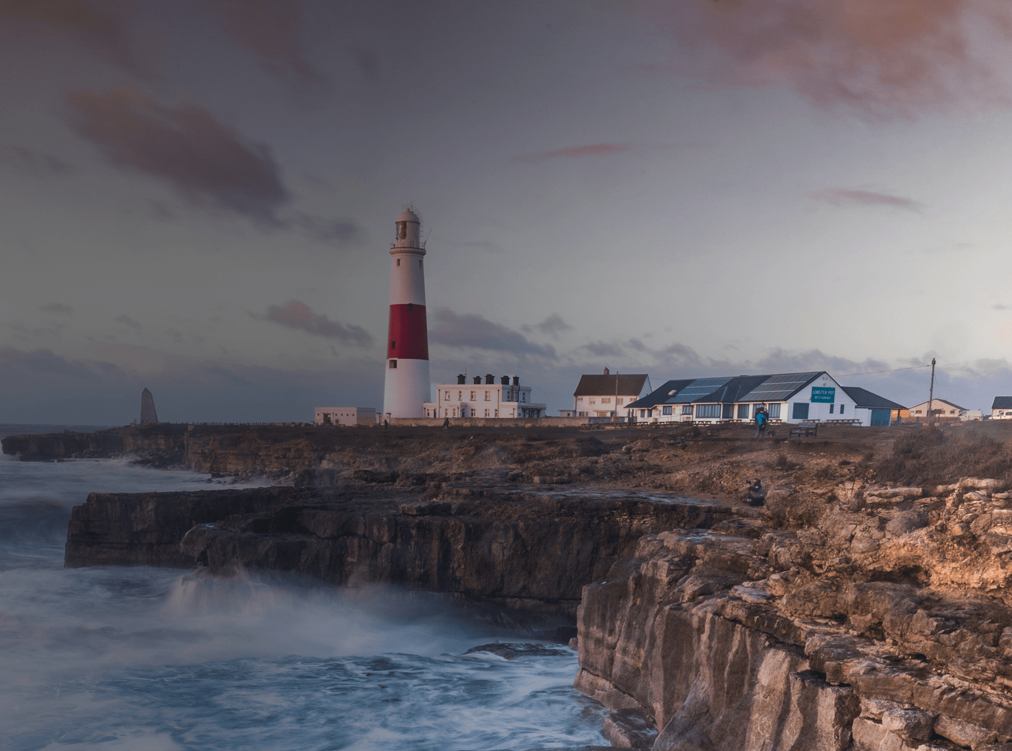 Las olas rompen en un acantilado británico con un faro en la distancia.