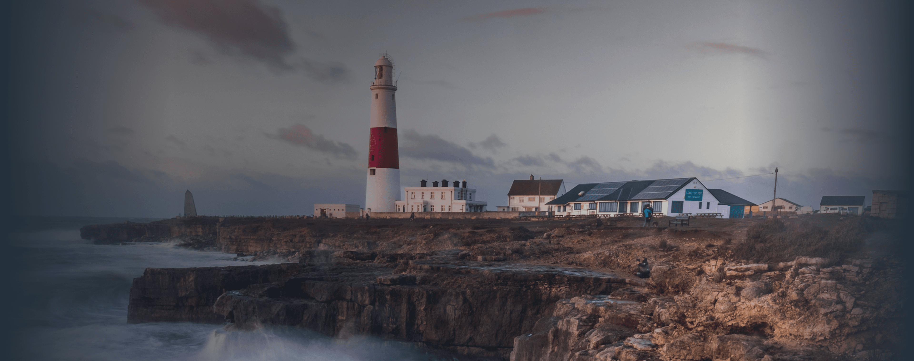 Las olas rompen en un acantilado británico con un faro en la distancia.