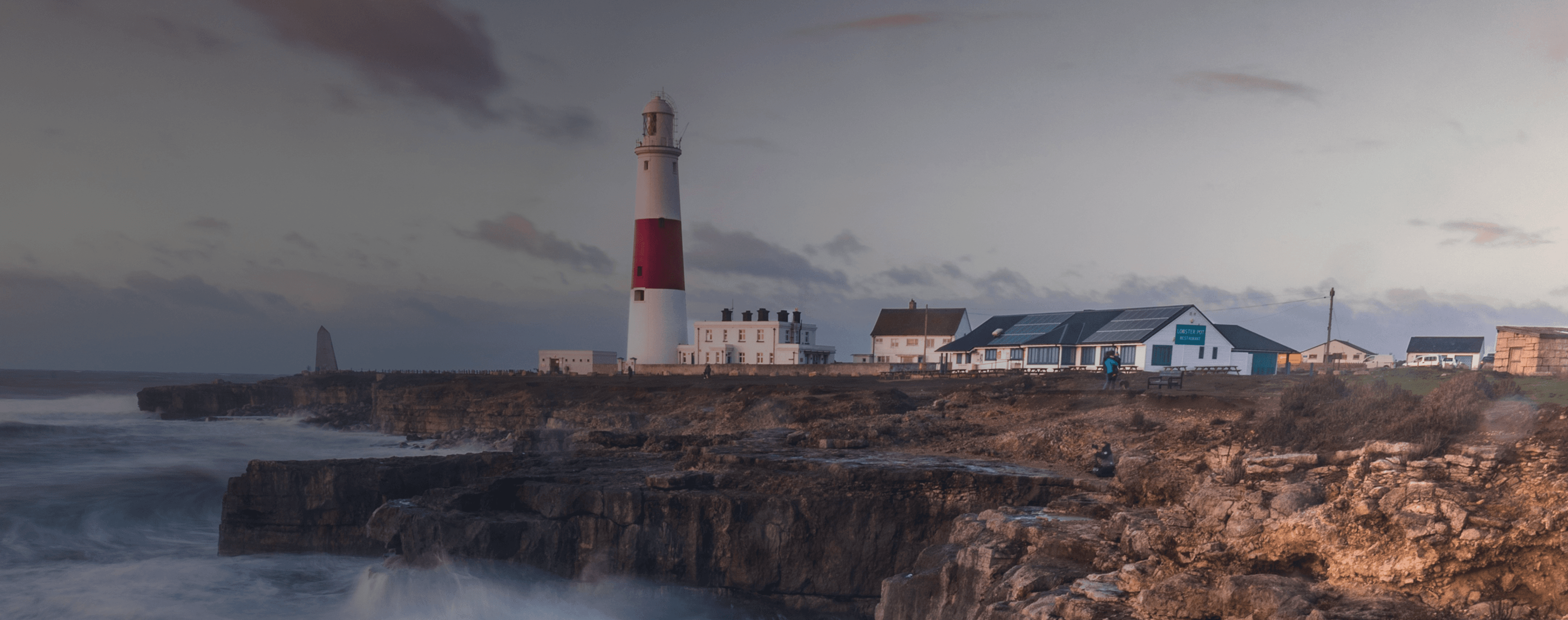 Las olas rompen en un acantilado británico con un faro en la distancia.