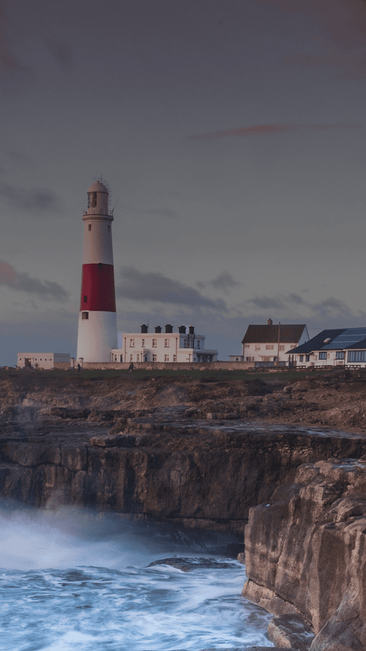 Las olas rompen en un acantilado británico con un faro en la distancia.